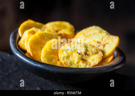 Le plantain poêlée de pièces dans une cuvette d'argile noir sur fond noir Banque D'Images