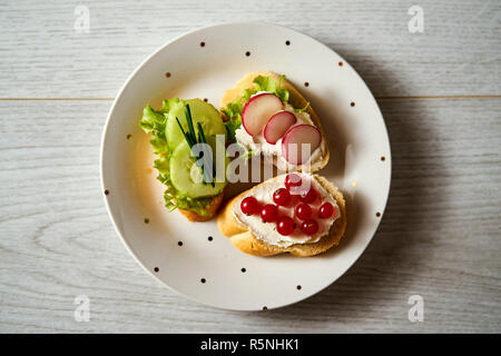 La plaque avec un ensemble de mini-sandwiches végétariens avec le concombre, le radis et la ciboulette sur une table en bois clair Banque D'Images