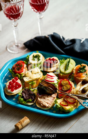 Ensemble de mini-sandwiches et tapas pour deux avec des verres de vin sur une table en bois clair Banque D'Images