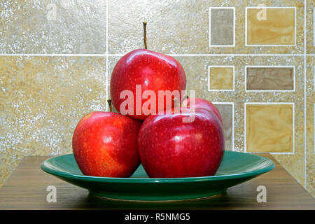 Les pommes d'un rouge brillant de variété Gala empilés sur une plaque verte placée sur une table en bois brun, close-up avec arrière-plan géométrique abstraite Banque D'Images