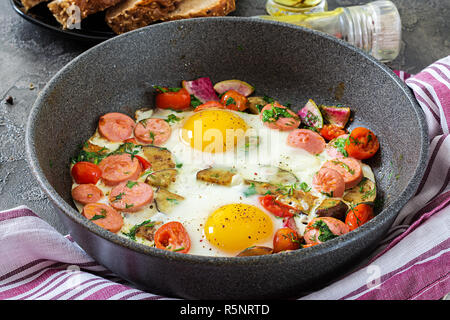 Poêle avec de délicieux oeufs, saucisses et légumes sur le tableau gris. Le petit-déjeuner. Banque D'Images