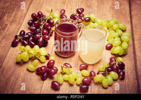 Verre de vin rouge et 2 verres d'stum stum blanc avec quelques raisins verts et rouges photpgraphed sur un morceau de bois de style rétro. Banque D'Images