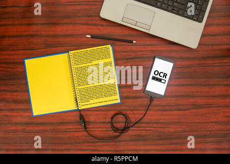 Voir ci-dessus d'un bloc-notes connecté à un smartphone via un câble USB sur un bureau. La reconnaissance optique de caractères barre de chargement. Banque D'Images