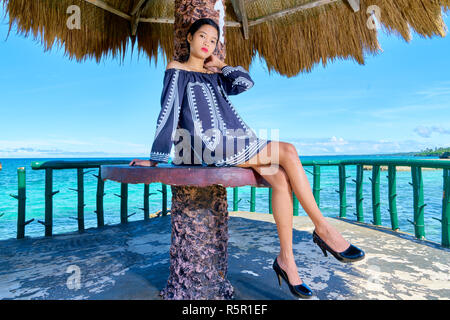 Beautiful woman posing - assis sur la table, les jambes croisées, les mains sur le cou Banque D'Images