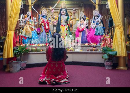 Une femme hindoue non identifiés s'agenouille dans la prière et la méditation en face des statues de divinités dans un temple dans le Queens, New York. Banque D'Images