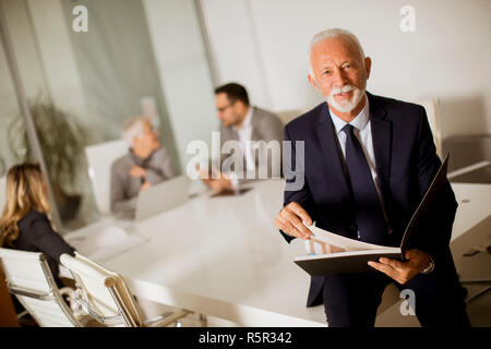 Portrait of senior woman standing in office tandis que d'autres businessman Banque D'Images