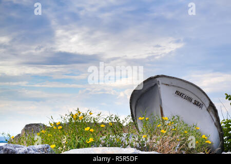 Vieux bateau en bois sur la rive entouré de fleurs jaunes, tourné à partir de l'angle inférieur. Banque D'Images