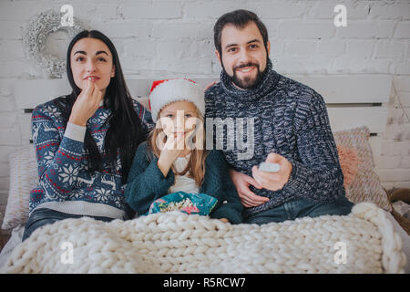 Joyeux Noël et Bonne Année . Jeune famille célèbre maison de vacances à la maison. Le père tient la télécommande du téléviseur. Père, mère et fille sont à regarder la télévision. Banque D'Images