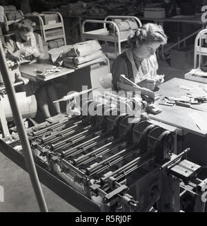 Années 1950, historiques, les femmes travaillant dans une usine industrielle, assis à de petites tables à côté des machines, England, UK. Banque D'Images