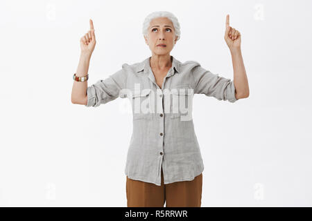 Studio shot of concernés hésitant et incertain perplexe vieille femme en chemise et pantalon à la pointe vers le haut et à l'expression inquiète pas sûr d'avoir Banque D'Images