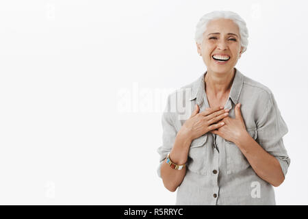 Vieille Femme insouciante heureux satisfait de comment va la vie. La haute dame charmante joyeuse avec des cheveux gris en chemise holding palms sur la poitrine et de rire Banque D'Images