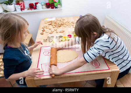 Une fille est à l'aide du rouleau à pâtisserie étalez la pâte sur la table pendant que sa soeur est à regarder Banque D'Images