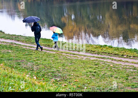 Mère avec son enfant marchant le long d'une rivière avec des parapluies dans un jour de pluie Banque D'Images
