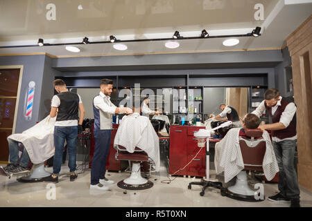 Vue de l'arrière du processus de travail en vintage barber shop. Coiffeurs qualifiés en chemises blanches et gilets avec barbe rasage rasoirs et faire une coupe à la mode. Concept de la coiffure. Banque D'Images