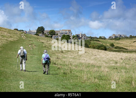 Couple de personnes âgées avec sacs à dos en direction du village pittoresque de Worth Matravers sur l'île de Purbeck, Dorset, Angleterre, Royaume-Uni Banque D'Images