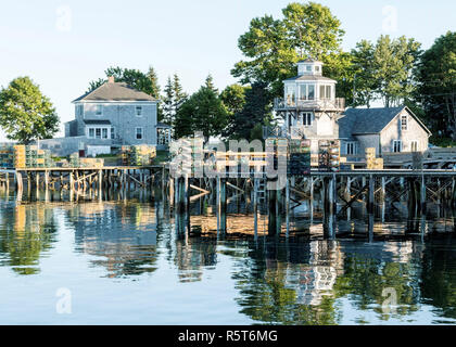 La côte de bass harbor Maine avec maisons, arbres, et leurs casiers à homard empilés sur les quais tous reflétant dans l'eau Banque D'Images