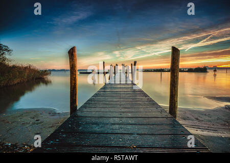 Belle matinée au bord du lac sur une longue jetée avec planches en bois, la rosée du matin et un lever du soleil. Banque D'Images