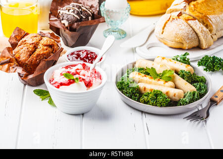 Petit déjeuner servi avec des muffins, des saucisses grillées, jus de fruits, pain frais et parfait sur une table en bois blanc, copie de l'espace. Banque D'Images