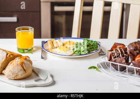 Petit-déjeuner servi avec les œufs, de la salade, des muffins et du jus d'orange sur la table en bois blanc, dans la cuisine. Banque D'Images