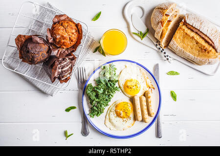 Petit-déjeuner servi avec les œufs, de la salade, des muffins et du jus d'orange sur la table en bois blanc, vue du dessus, copiez l'espace. Banque D'Images