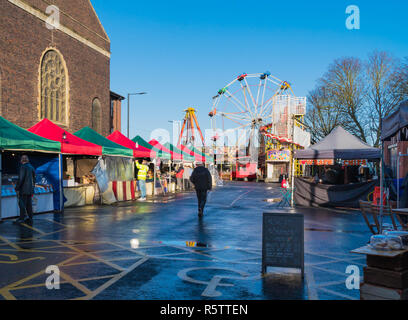 Trader dans la veste Hi-vis de mise en place de la stalle avec la roue de Ferris et le squelette de Helter en arrière-plan. Foire de Noël victorienne de Worcester. Worcestershire U. Banque D'Images