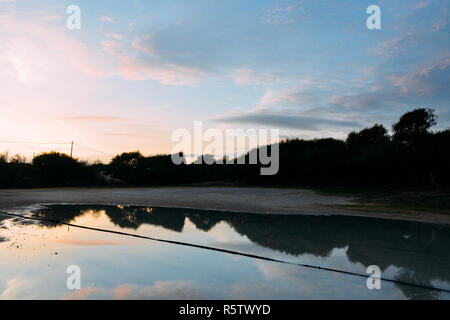 Belles, lumineuses et vives, saturées, coucher de soleil aux couleurs orange, rose, bleu et violet des nuages dans le ciel au-dessus de la réflexion sur les flaques de pluie. Banque D'Images