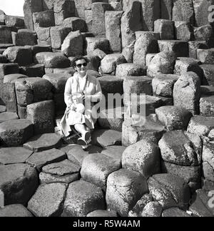 Années 1950, historiques, une femme assise sur les anciennes colonnes de basalte volcanique à la Giant's Causeway en Co. d'Antrim, en Irlande du Nord. À la côte de l'Atlantique Nord, la chaussée est une merveille géologique, une zone de 40 000 colonnes de basalte d'enclenchement, le résultat d'une ancienne fissure volcanique éruption. Banque D'Images