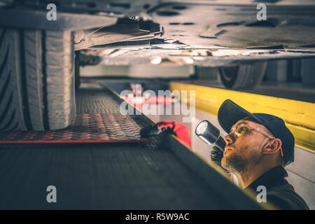 Suspension voiture Question. Mécanicien de véhicules de race blanche avec torche Inspecting car le train roulant. Banque D'Images