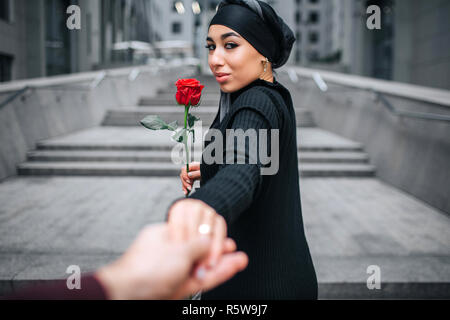 Belle photo de jeunes arabian woman hold rose rouge et regarder en arrière. Elle sent. Attente modèle main. Elle sourit Banque D'Images