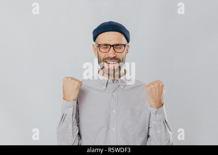 Signe de succès. Jubilant de joie l'homme non rasé soulève les poings serrés, porte des lunettes et maillot officiel, célèbre son triomphe, ferme les yeux à partir de Banque D'Images