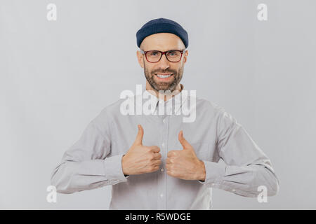 J'aime cette idée ! Heureux l'homme non rasé soulève Thumbs up, sourit largement, satisfait de grand choix, a dark chaume, habillé de shirt, isolé Banque D'Images