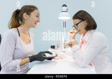 Young smiling woman esthéticienne manucure parlant à une cliente, n'manucure, femme choisir une couleur de vernis à ongles. Banque D'Images