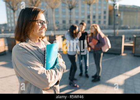 Portrait of mature female teacher dans les verres avec des presse-papiers, piscine avec un groupe d'Adolescents Étudiants, heure d'or. Banque D'Images