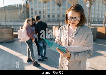 Portrait of mature female teacher dans les verres avec des presse-papiers, piscine avec un groupe d'Adolescents Étudiants, heure d'or. Banque D'Images