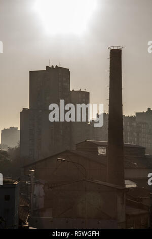 Ancienne cheminée en brique d'une usine abandonnée, à partir de la révolution industrielle, tandis qu'un bloc d'habitation yougoslave socialiste construire tour peut être vu dans t Banque D'Images
