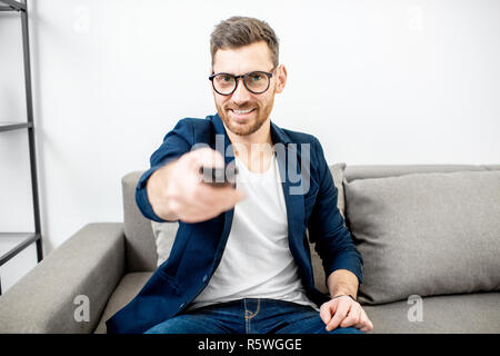 Businessman habillé de commutation avec désinvolture plat channles avec télécommande sur le canapé à la maison Banque D'Images