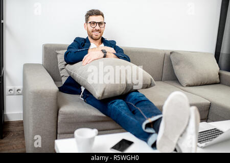 Businessman habillés à la légère détente sur le canapé tout en regardant la TV à la maison Banque D'Images