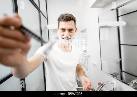 Portrait d'un homme en blanc T-shirt shawing avec lame et la mousse dans la salle de bains Banque D'Images