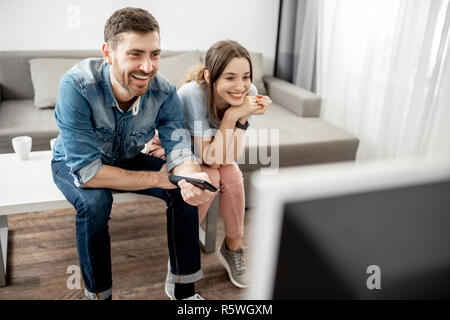 Jeune couple avec de belles émotions heureux de regarder la télévision, assis sur la table à la maison Banque D'Images