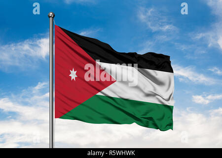 Brandissant le drapeau de la Jordanie dans le vent contre blanc nuageux ciel bleu. Drapeau jordanien. Banque D'Images