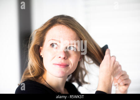 Femme debout dans la salle de bains se coiffant Banque D'Images