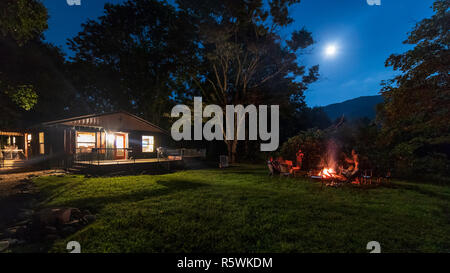 Groupe de personnes autour d'un feu de camp dans la forêt sous une nuit éclairée par la lune Banque D'Images