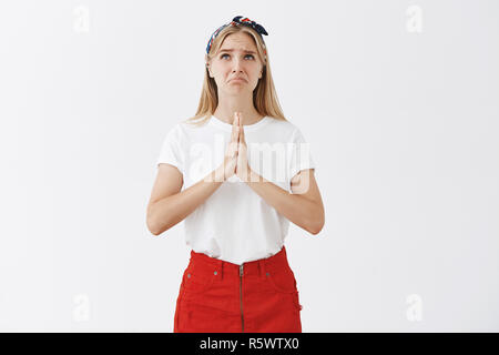 Studio shot of déplut funny européennes avec juste les cheveux en bandeau et jupe, fronçant et recherche de lèvres tout en tenant les mains dans la prière sur la poitrine, Banque D'Images