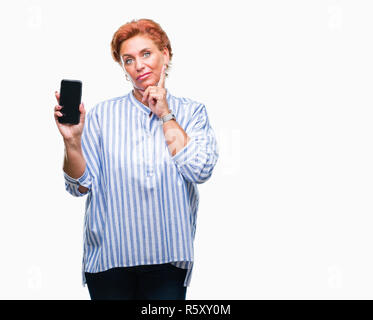 Atrractive young redhead femme montrant l'écran du smartphone sur fond isolé visage sérieux de penser à question, idée très confus Banque D'Images