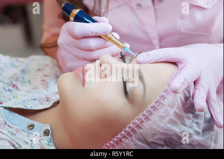 Une jeune femme se trouve et récupère un de ses sourcils dans un salon de beauté. L'utilisation de maquillage permanent sur les sourcils. Le maître travaille avec les sourcils. Maquillage semi-permanent Banque D'Images