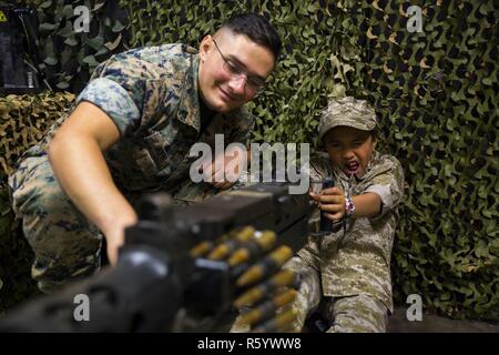 Corps des Marines des États-Unis Le Cpl. Jeffery Aceti, gauche, ingénieur de combat avec l'Escadron de soutien de l'aile Marine (MWSS) 171, aide Cosme Rosete, un jour recruter Junior participant, avec l'adresse au tir simulé à l'intérieur de l'entraîneur de calibre .50 M2 heavy machine gun-Marine au cours de groupe d'aéronefs 12 Recruter Junior Journée au Marine Corps Air Station Iwakuni, Japon, le 21 avril 2017. L'objectif de recruter 24 Junior est d'accroître l'état de préparation de la famille dans la communauté en montrant les enfants et les jeunes adultes qui sont ses parents sur une base quotidienne. Banque D'Images