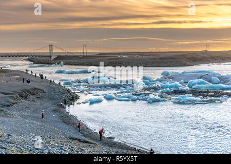 Islande - 5 novembre 2017 - Un groupe de touristes et habitants à prendre des photos de la lagune glaciaire du Jökulsárlón, un avec un coucher de soleil et d'un pont dans le background Banque D'Images