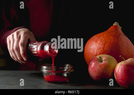 Bouteille avec canneberge dans la main, la citrouille et les pommes sur la table Banque D'Images