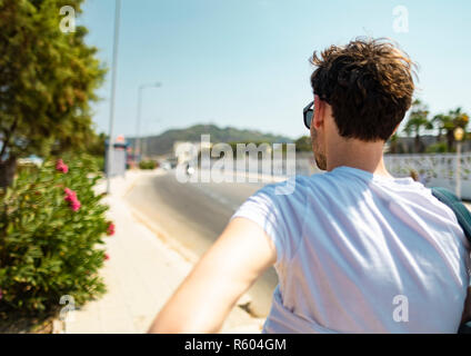 Tiré de l'arrière d'un jeune homme de race blanche blanc portant des lunettes et un T shirt blanc, marchant sur une route vers les montagnes sur une île grecque en G Banque D'Images