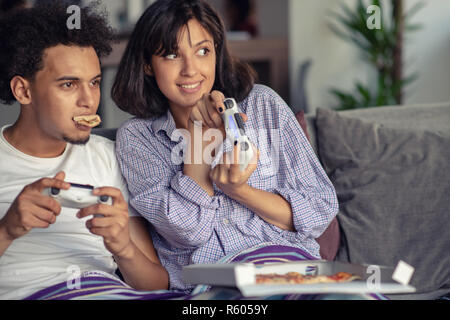 Image de jeune couple aimant dans la cuisine à la maison à l'intérieur. Eating pizza et jouer à des jeux avec la console. Banque D'Images